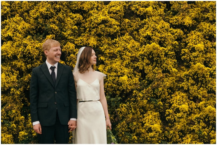 bride and groom with a wall of wild yellow flowers 