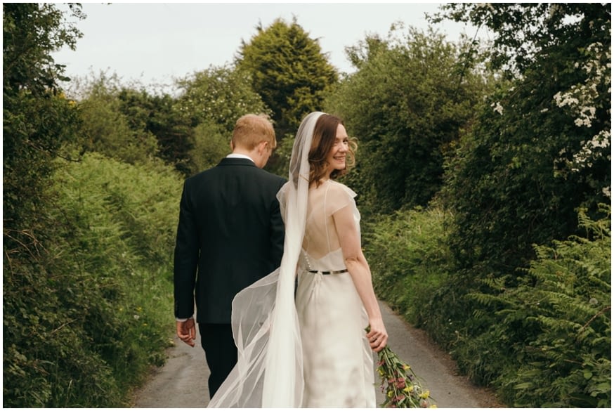 Bride and groom walk down country lane 