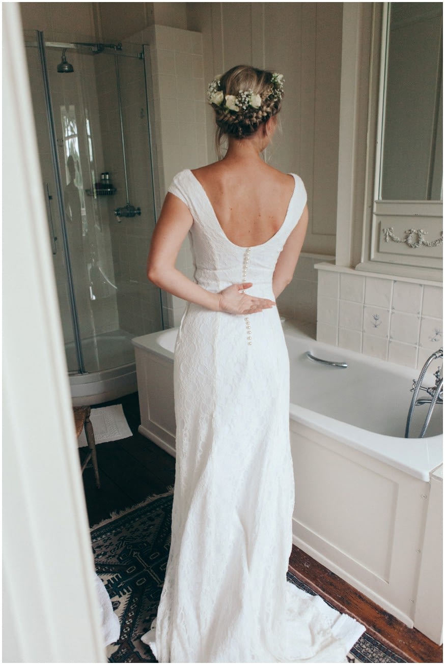 Bride with grecian braid and flowers in her hair checks herself in the mirror 