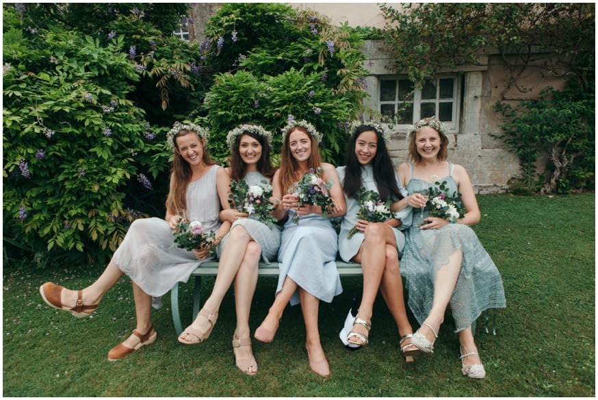 Bridesmaids in light pastel green dresses sit in flower garden 