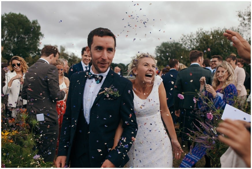 Bride and groom walk down the aisle while guests through flower petal confetti 