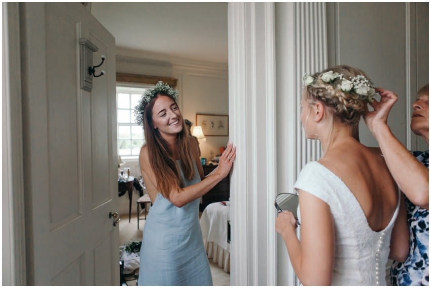 Bridesmaid with flowers in her hair watches as Bride gets ready 